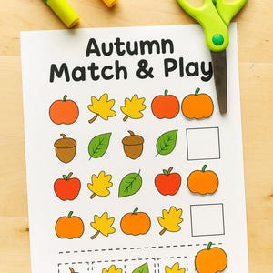 Puede incluir: Una hoja de trabajo impresa titulada "Autumn Match & Play" con ilustraciones coloridas de manzanas, hojas, bellotas y calabazas. También hay marcadores verdes y amarillos y tijeras verdes.