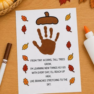 May include: A white paper craft sheet featuring a brown handprint centered below a brown acorn illustration. The text reads: FROM TINY ACORNS, TALL TREES GROW, I'M LEARNING NEW THINGS AS I GO. WITH EVERY DAY, I'LL REACH UP HIGH, LIKE BRANCHES STRETCHING TO THE SKY.