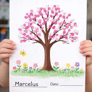 May include: A child holds a white paper with a tree illustration. The tree has a brown trunk and branches with pink and white fingerprint leaves. Colorful flowers and a yellow butterfly are at the base. The name "Marcelus" is written at the bottom.