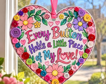 May include: A heart-shaped hanging sign with a pink ribbon, featuring colorful floral illustrations and the text "Every Button Holds a Little Piece of My Love!" The border is decorated with various multicolored plastic buttons.