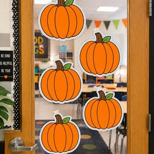 Puede incluir: Cinco recortes de calabaza de color naranja con tallos marrones y hojas verdes están pegados en una puerta de cristal. Cada calabaza presenta un borde blanco discontinuo y está sujeta con un pequeño trozo de cinta adhesiva blanca.