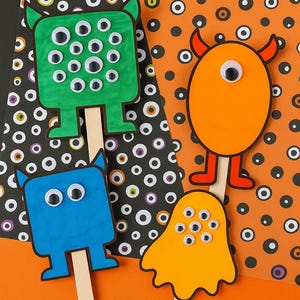May include: Four colorful monster-shaped craft sticks. The monsters are green, blue, orange, and yellow, with googly eyes and stick legs. The background is orange and black with a polka dot pattern.