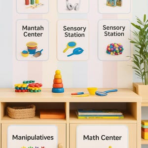 Op de afbeelding: Een houten speelcentrum met gelabelde activiteitencentra. De centra omvatten Kunst, Wetenschap, Bibliotheek, Mantah en Sensorisch. De onderste laag heeft Manipulatives en Math Center. Speelgoed: kleurrijke blokken, boeken en een stapelring.