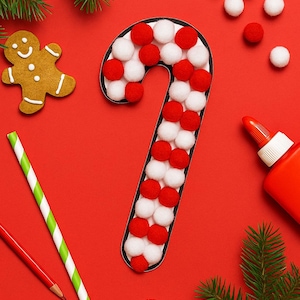 May include: A festive Christmas-themed arrangement on a red background. A candy cane shape is decorated with red and white pom-poms. Other elements include a gingerbread man, a green and white striped straw, and a red pencil.