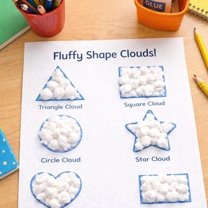 May include: A worksheet titled "Fluffy Shape Clouds!" features shapes filled with cotton balls: triangle, square, circle, star, heart, and rectangle. A red cup of colored pencils, glue, scissors, and a notepad are also visible.
