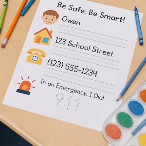 Puede incluir: Un papel blanco con el texto "Be Safe, Be Smart!" e información de contacto, incluyendo un nombre, dirección y número de teléfono. El papel está rodeado de lápices de colores y una paleta de acuarelas sobre una superficie de madera.