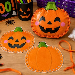 May include: A craft kit featuring three orange pumpkin shapes with green stems. One pumpkin is assembled into a three-dimensional form with orange ribbon lacing, while two flat pumpkin cutouts feature pre-punched holes along the edges.