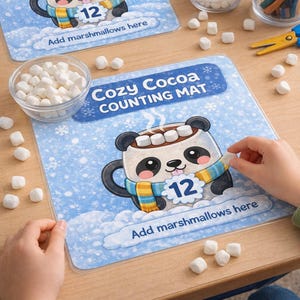 May include: A blue counting mat with a cartoon panda mug design. The mat features the text "Cozy Cocoa COUNTING MAT" and "Add marshmallows here". The mug has the number 12 on it. Marshmallows and colored pencils are also visible.