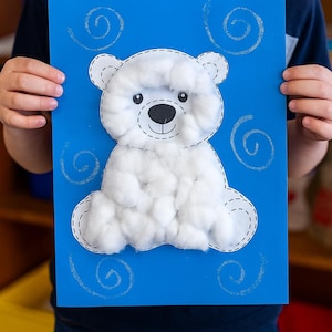 May include: A handmade polar bear craft on a blue background. The bear is made of white cotton balls and has a black nose and eyes. The outline is stitched with black thread. Swirls are drawn in silver on the blue background.