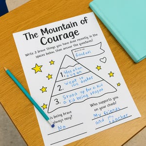 May include: A worksheet titled "The Mountain of Courage" with a mountain graphic, stars, and the text "Good adl". A teal pencil and a teal book are on a wooden desk.
