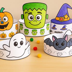 Può includere: Una collezione di cerchietti di carta a tema Halloween, con una zucca sorridente, il mostro di Frankenstein, un cappello da strega, un fantasma e un pipistrello. I cerchietti sono decorati con illustrazioni colorate e circondati da pompon e pennarelli colorati.
