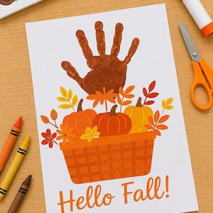 Op de afbeelding: Een wit vel papier met een bruine handafdruk in de vorm van een boom boven een mand vol oranje en gele pompoenen en herfstbladeren. De tekst Hello Fall! is in het oranje onderaan de papieren illustratie gedrukt.