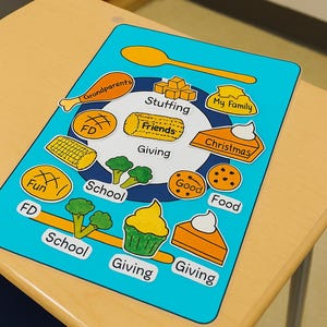 May include: A blue educational placemat with illustrations of food and words like "Friends," "School," and "Giving." The placemat is on a wooden desk, and the illustrations include a cupcake, pie, and broccoli.