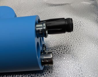 May include: A close-up of a blue cylindrical object with multiple openings. A black, cylindrical component is inserted into one opening. Another opening has a silver-colored component. The background is a shiny, silver surface.