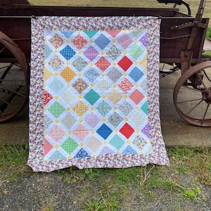 Peut inclure: Une courtepointe rectangulaire présentant un motif en patchwork de losanges avec divers carrés de tissu à motifs floraux, unis et géométriques multicolores. La courtepointe est bordée d'un tissu à motif floral vif et de petits carrés jaunes.