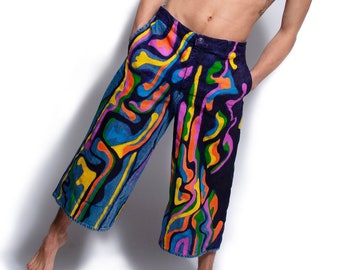 May include: A person wearing blue denim pants with a colorful abstract pattern. The pants have a wide leg and are cropped above the ankles.