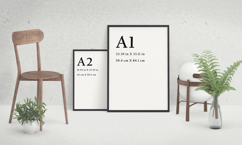May include: Two framed art prints with black borders, labeled A1 and A2, with dimensions in inches and centimeters. A wooden chair and a decorative plant are on the left. A white sphere on a wooden stand and a vase with greenery are on the right.