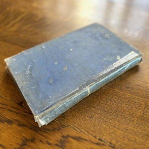 May include: A blue, worn, hardcover book with a faded, textured cover.