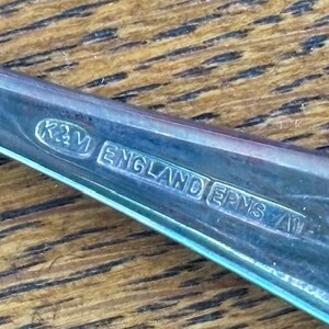Puede incluir: Primer plano de un utensilio de plata con la inscripci&oacute;n "K&M ENGLAND EPNS A1" en la parte posterior.