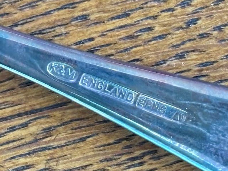 Puede incluir: Primer plano de un utensilio de plata con la inscripci&oacute;n "K&M ENGLAND EPNS A1" en la parte posterior.