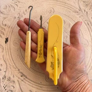 May include: Set of three vintage yellow plastic sewing tools with floral designs. The tools include a hook, a needle threader, and a button hook.