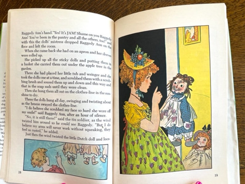 Puede incluir: Una ilustraci&oacute;n vintage de una ni&ntilde;a con cabello rojo y un vestido amarillo sosteniendo una mu&ntilde;eca de trapo. La mu&ntilde;eca de trapo lleva un vestido azul con un delantal blanco. La ni&ntilde;a est&aacute; se&ntilde;alando a la mu&ntilde;eca de trapo y diciendo "&iexcl;S&iacute;! &iexcl;Es mermelada!" La ilustraci&oacute;n es de un libro infantil.