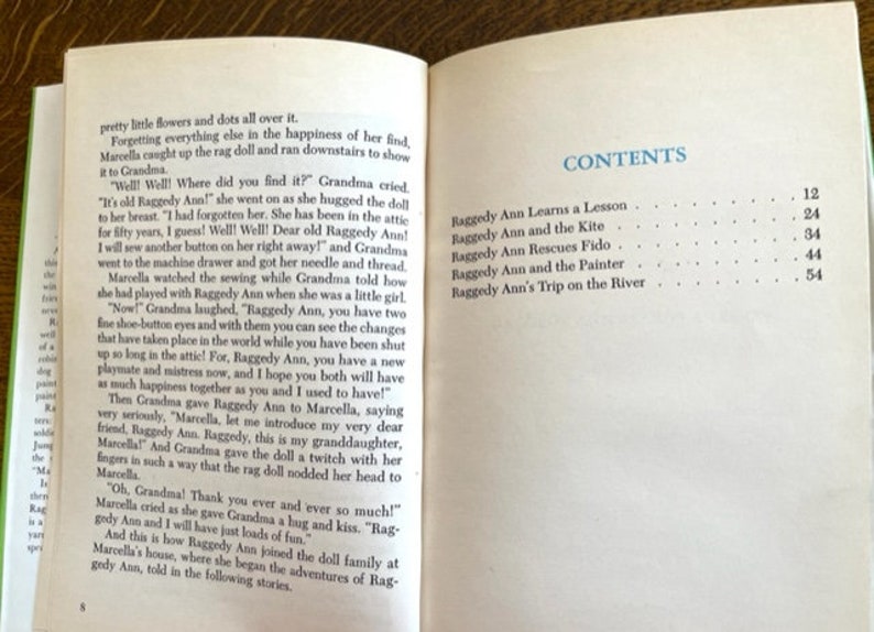 Puede incluir: Un libro titulado "Raggedy Ann" con una tabla de contenido que enumera los cap&iacute;tulos y los n&uacute;meros de p&aacute;gina. Los cap&iacute;tulos incluyen "Raggedy Ann aprende una lecci&oacute;n", "Raggedy Ann y la cometa", "Raggedy Ann rescata a Fido", "Raggedy Ann y el pintor", y "El viaje de Raggedy Ann por el r&iacute;o".