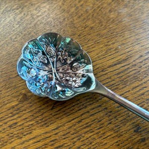 Puede incluir: Una cuchara de plata con un dise&ntilde;o floral decorativo en el cuenco. La cuchara tiene un mango largo y delgado.