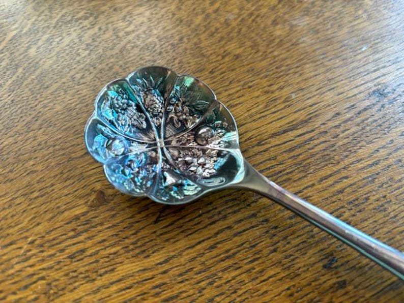 Puede incluir: Una cuchara de plata con un dise&ntilde;o floral decorativo en el cuenco. La cuchara tiene un mango largo y delgado.