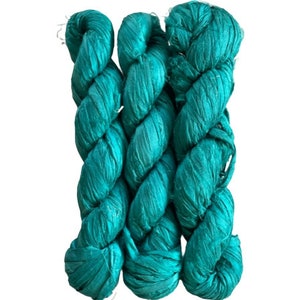 May include: Three skeins of vibrant teal silk ribbon yarn arranged vertically. Each skein features a lustrous, crinkled texture with a consistent deep turquoise color throughout, showcasing a flat, wide ribbon construction with frayed edges.