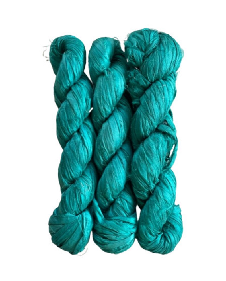 May include: Three skeins of vibrant teal silk ribbon yarn arranged vertically. Each skein features a lustrous, crinkled texture with a consistent deep turquoise color throughout, showcasing a flat, wide ribbon construction with frayed edges.