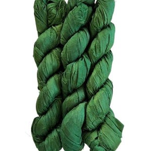 May include: A bundle of emerald green silk ribbon yarn featuring a crinkled, textured surface. The material is wound into a long, twisted skein with frayed edges visible along the length of the fabric strips, showcasing a consistent deep green hue.