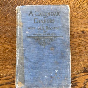May include: A blue hardcover book titled "A Calendar of Dinners with 615 Recipes" by Marion Harland.
