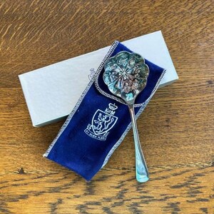 Puede incluir: Una cuchara de servir de plata con un dise&ntilde;o floral decorativo. La cuchara est&aacute; en una bolsa de terciopelo azul con un escudo que dice "E.P. Silver Plate".