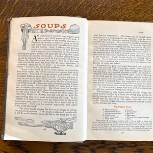 May include: An open vintage cookbook with a black and white illustration of a soup ladle and a bowl of soup on the left page. The right page has a recipe for Asparagus Soup with a list of ingredients and instructions.