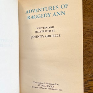 Puede incluir: Una portada de libro vintage con el t&iacute;tulo "Adventures of Raggedy Ann" escrito en azul sobre un fondo crema. El autor e ilustrador, Johnny Gruelle, aparece debajo del t&iacute;tulo. El libro est&aacute; publicado por Avenel Books, una divisi&oacute;n de Crown Publishers, Inc.