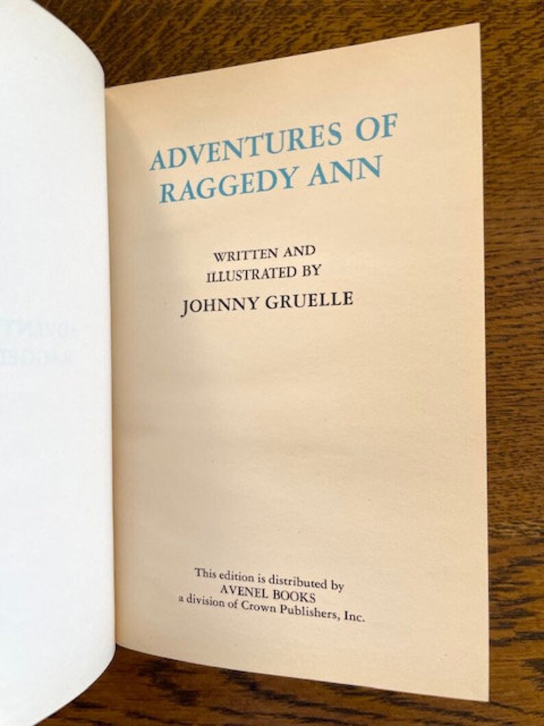 Puede incluir: Una portada de libro vintage con el t&iacute;tulo "Adventures of Raggedy Ann" escrito en azul sobre un fondo crema. El autor e ilustrador, Johnny Gruelle, aparece debajo del t&iacute;tulo. El libro est&aacute; publicado por Avenel Books, una divisi&oacute;n de Crown Publishers, Inc.
