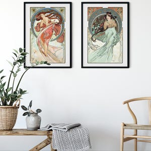 Puede incluir: Dos grabados enmarcados de estilo Art Nouveau que representan a mujeres elegantes con cabello y vestidos fluidos. La obra de arte tiene un dise&ntilde;o circular con elementos florales y decorativos. Los grabados est&aacute;n en marcos negros y cuelgan de una pared blanca.