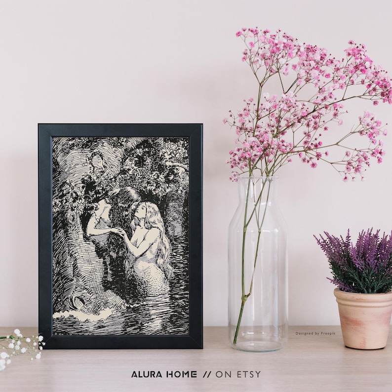 May include: A framed black and white print depicting a mermaid and a person in a forest setting. The print is displayed on a light-colored surface, next to a vase of pink flowers and a small potted plant. The text "ALURA HOME // ON ETSY" is at the bottom.