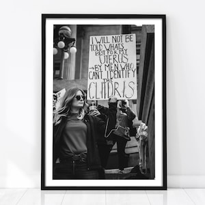 Könnte beinhalten: Ein Schwarz-Weiß-Foto eines Protestschildes, das in einer Menschenmenge hochgehalten wird. Das Schild zeigt handgeschriebenen Text: I WILL NOT BE TOLD WHAT'S BEST FOR MY UTERUS BY MEN WHO CAN'T IDENTIFY THE CLITORIS. Das Bild ist schwarz gerahmt.