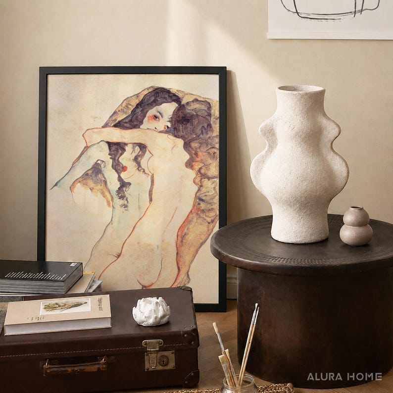 K&ouml;nnte beinhalten: Ein gerahmter Kunstdruck mit zwei sich umarmenden Figuren, eine gro&szlig;e, strukturierte, cremewei&szlig;e Keramikvase mit geschwungener Silhouette, eine kleine runde beige Vase, ein brauner Vintage-Koffer, ein B&uuml;cherstapel und ein kleines wei&szlig;es Deko-Objekt.