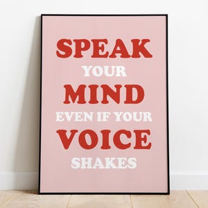 Può includere: Una stampa artistica incorniciata con le parole "SPEAK YOUR MIND EVEN IF YOUR VOICE SHAKES" in lettere rosse e bianche su sfondo rosa. La stampa è in una cornice nera.
