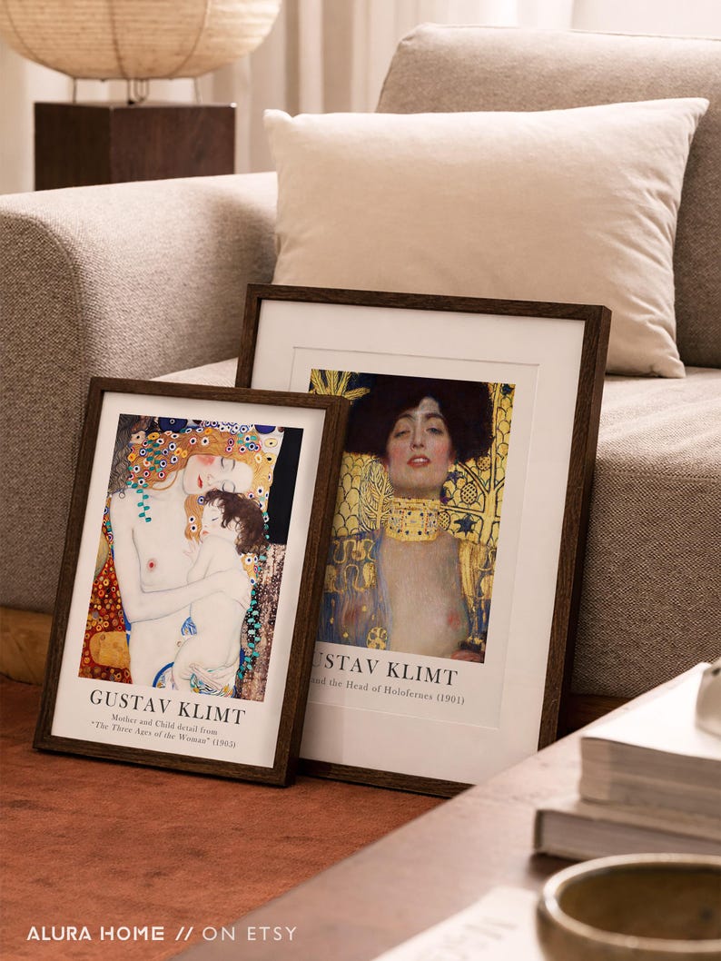 May include: Two framed art prints featuring Gustav Klimt paintings. The left print shows Mother and Child from The Three Ages of Woman, and the right print shows Judith and the Head of Holofernes. Both have dark wood frames and white matting.
