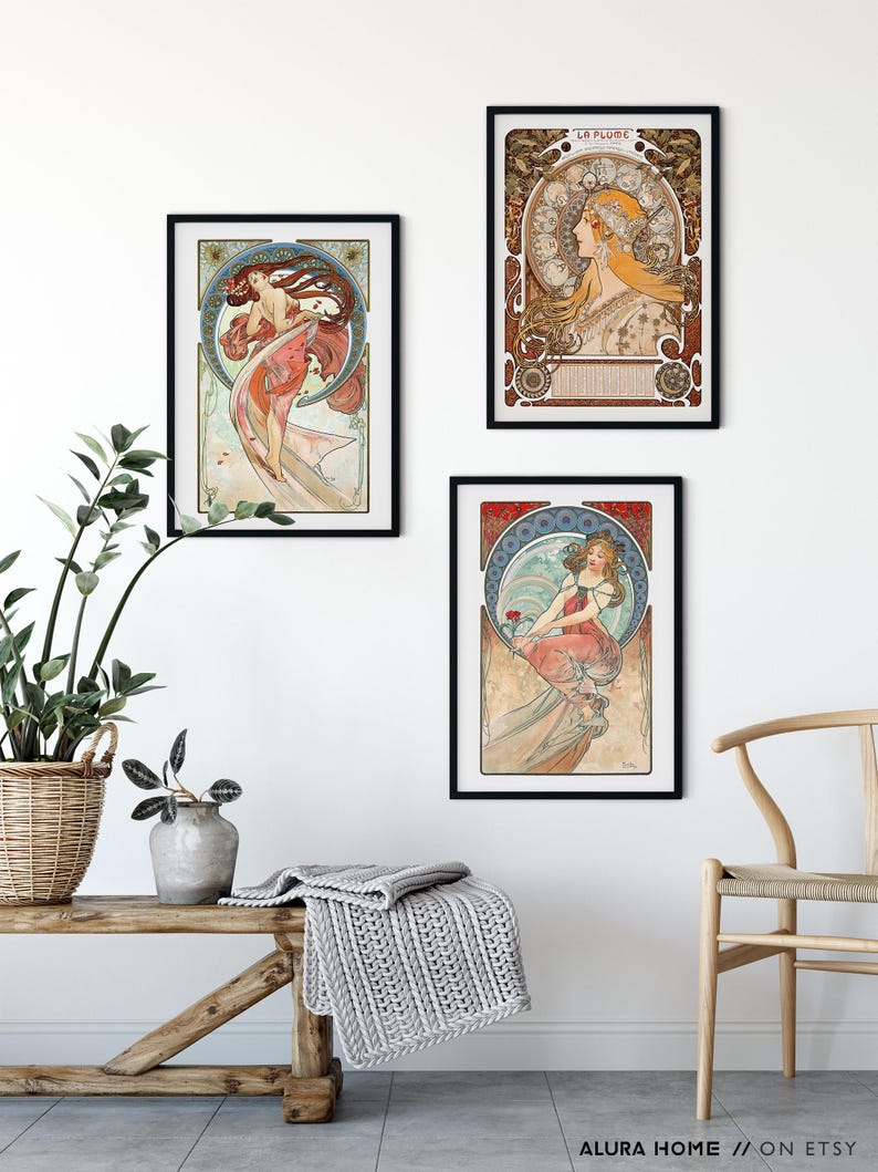 Puede incluir: Tres l&aacute;minas art&iacute;sticas enmarcadas con ilustraciones al estilo de Alphonse Mucha de mujeres con prendas fluidas y fondos circulares complejos, expuestas en marcos negros sobre una pared blanca encima de un banco de madera con una manta gris.