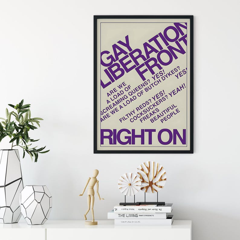 May include: A framed poster with a cream background and purple text that reads GAY LIBERATION FRONT, ARE WE A LOAD OF SCREAMING QUEENS? YES! ARE WE A LOAD OF BUTCH DYKES? YES! FILTHY REDS? YES! COCKSUCKERS? YEAH! FREAKS BEAUTIFUL PEOPLE RIGHT ON.