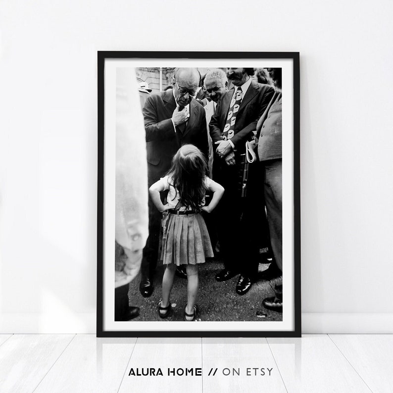 Peut inclure: Tirage encadr&eacute; en noir et blanc repr&eacute;sentant une jeune fille, les mains sur les hanches, face &agrave; un groupe d'hommes en costume. La photo capture un moment de la vie. L'impression est d'Alura Home sur Etsy.