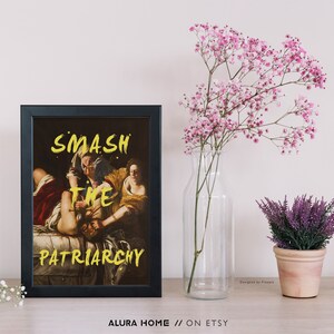 Puede incluir: Una impresi&oacute;n enmarcada en negro con una pintura de dos mujeres. La pintura es una reproducci&oacute;n de una obra de arte famosa. El texto "SMASH THE PATRIARCHY" est&aacute; escrito en pintura amarilla sobre la pintura.