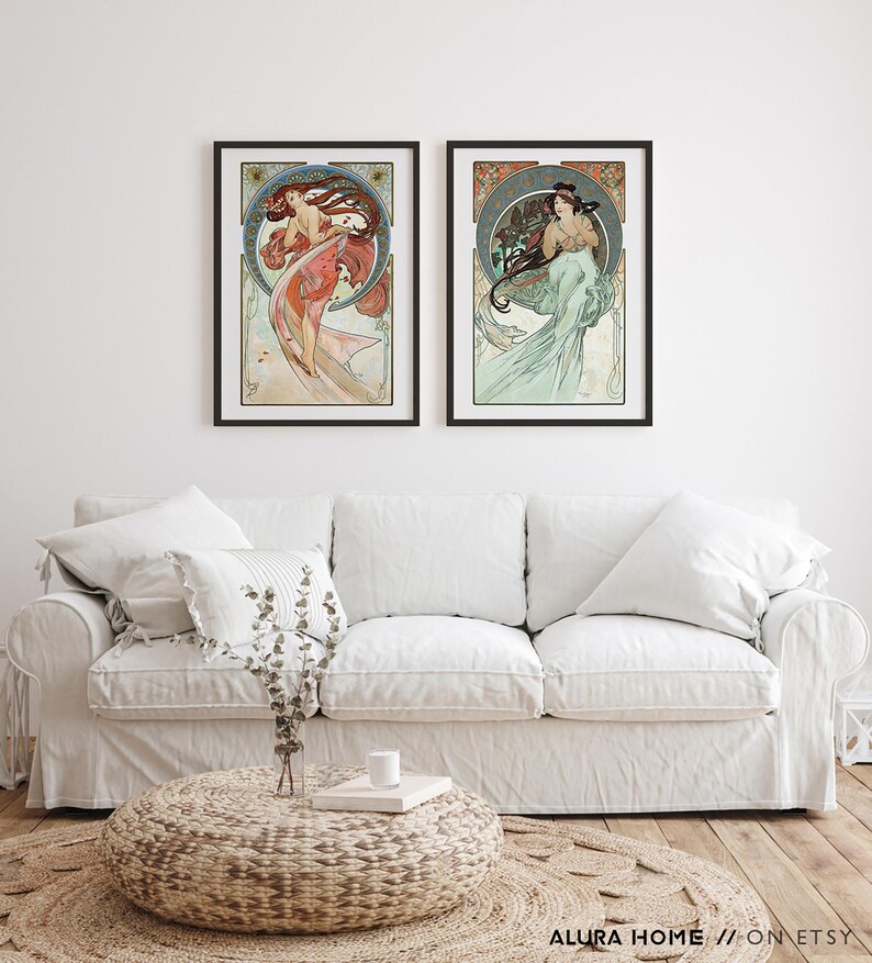 Puede incluir: Dos impresiones art&iacute;sticas enmarcadas con ilustraciones de estilo Art Nouveau de mujeres con cabello y vestidos fluidos. La obra de arte tiene una est&eacute;tica vintage con una paleta de colores de rojos, verdes y azules. Las impresiones se exhiben sobre un sof&aacute; blanco.