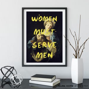 May include: Framed art print featuring a Renaissance-style painting with the text "WOMEN MUST SERVE MEN" in yellow. The artwork depicts a woman holding a platter with a man's head. The print is in a black frame.