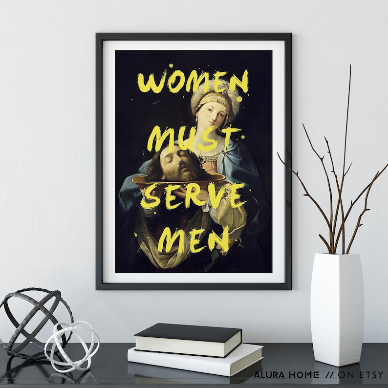 May include: Framed art print featuring a Renaissance-style painting with the text "WOMEN MUST SERVE MEN" in yellow. The artwork depicts a woman holding a platter with a man's head. The print is in a black frame.